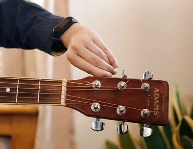 Guitar player tuning an acoustic guitar headstock in standard E